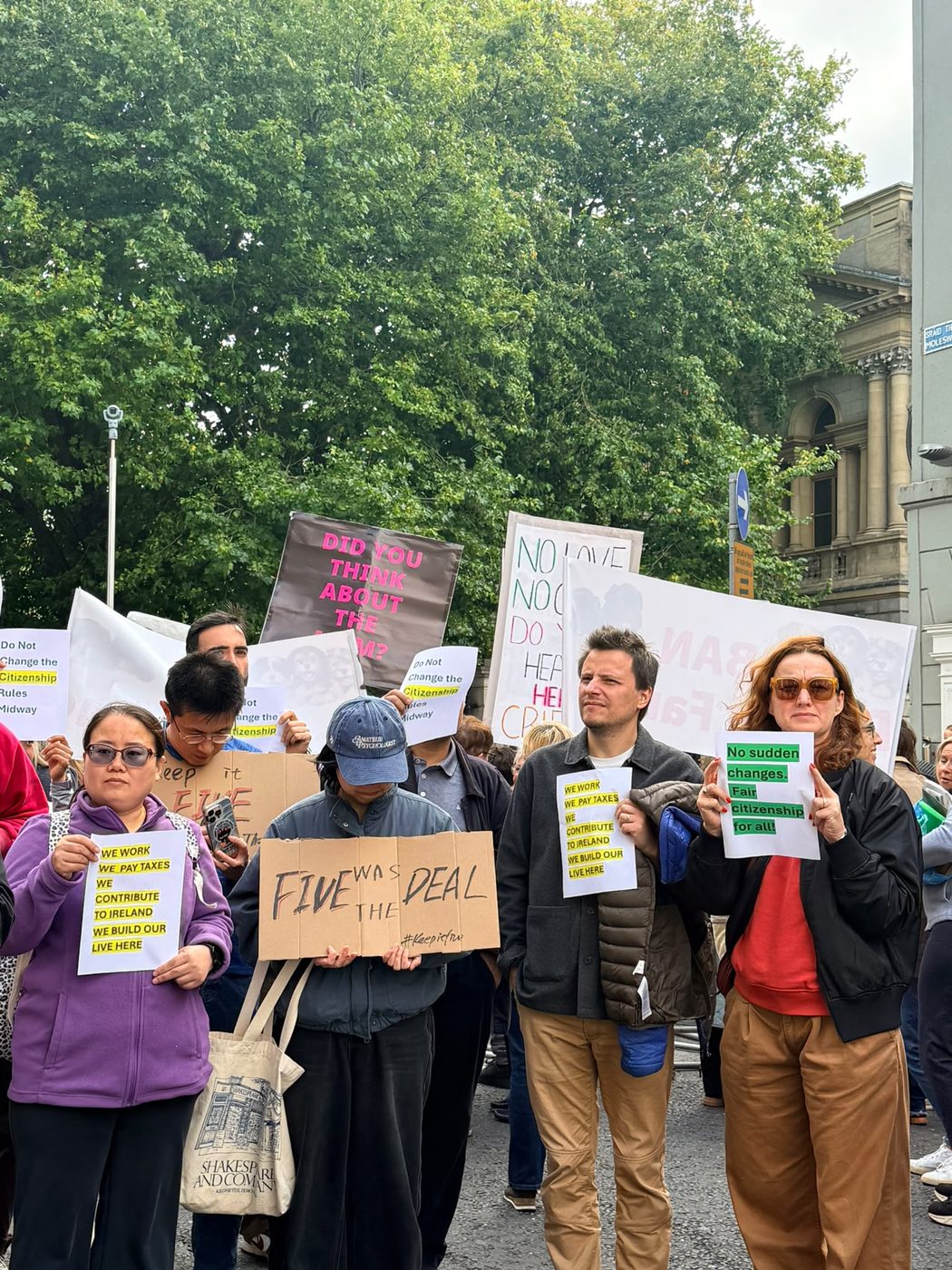 A cardboard sign reading ‘Five was the deal’, beside one reading ‘We work, we pay taxes, we contribute to Ireland, we build our lives here’
