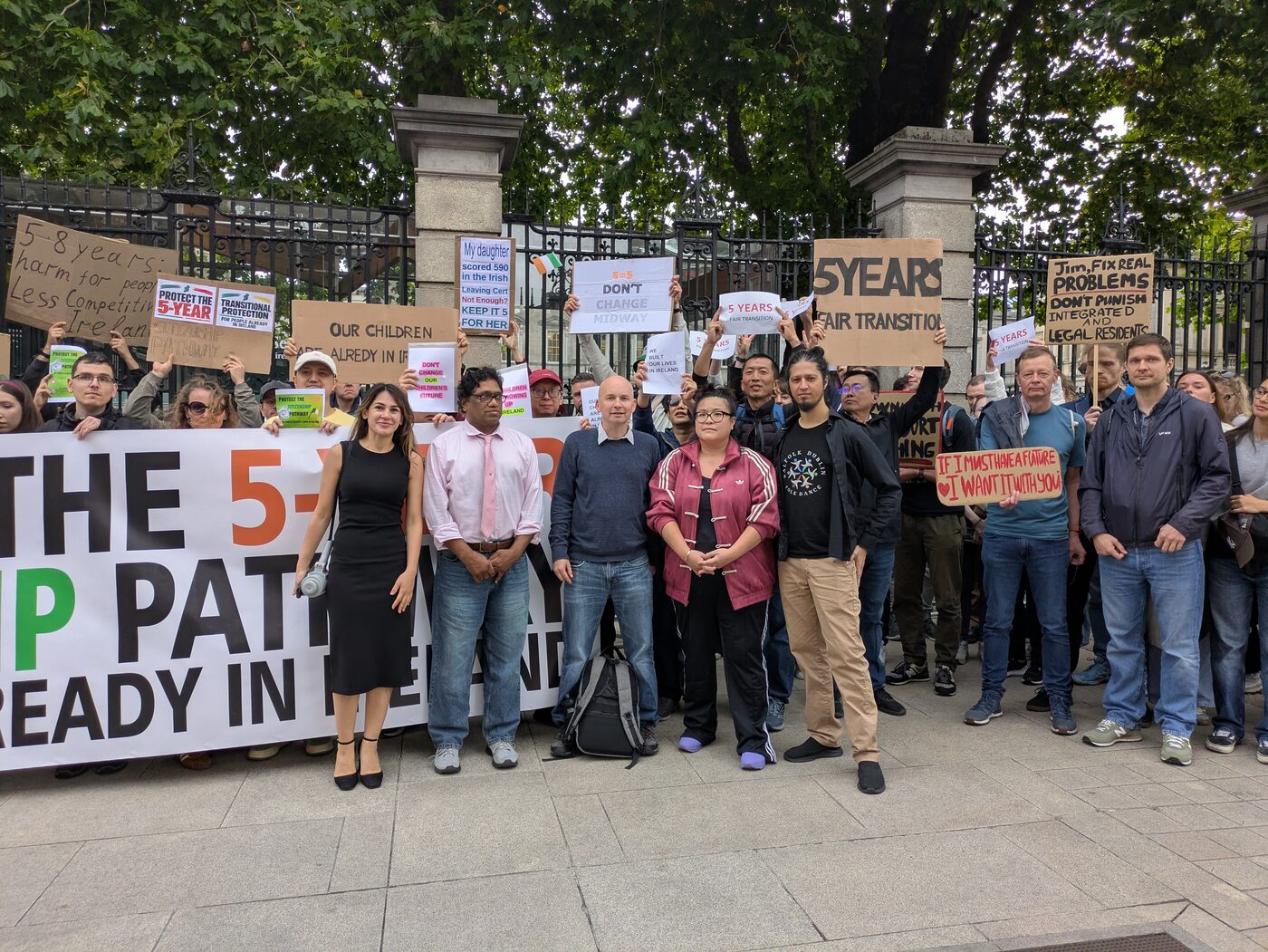 The whole gathering at the gates of Leinster House behind the banner, with signs reading ‘Jim, fix real problems, don’t punish integrated and legal residents’ and ‘If I must have a future, I want it with you’